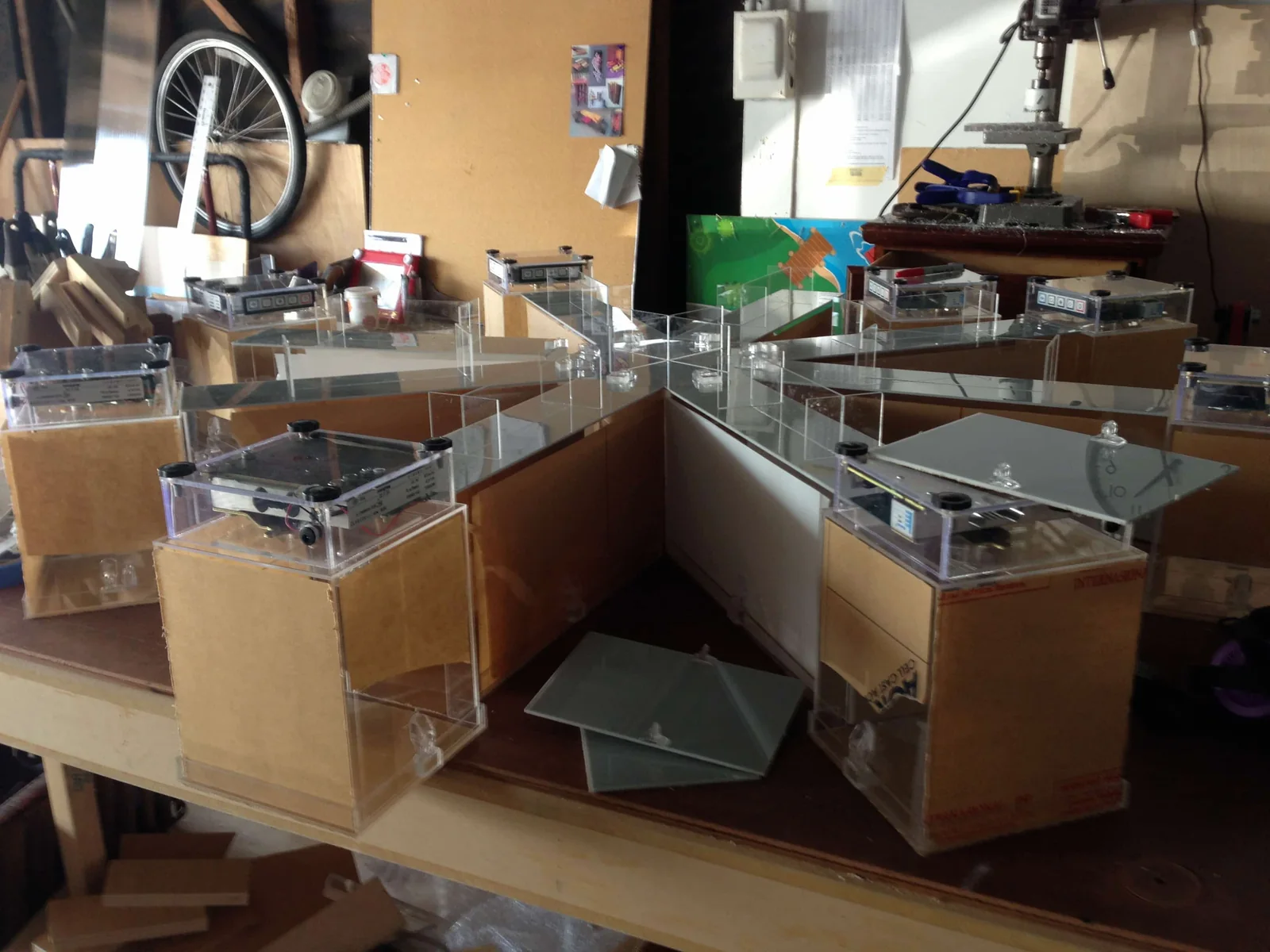 A clear acrylic eight-arm radial maze on a wooden workbench, each arm ending in a box topped by a clear case holding circuit boards