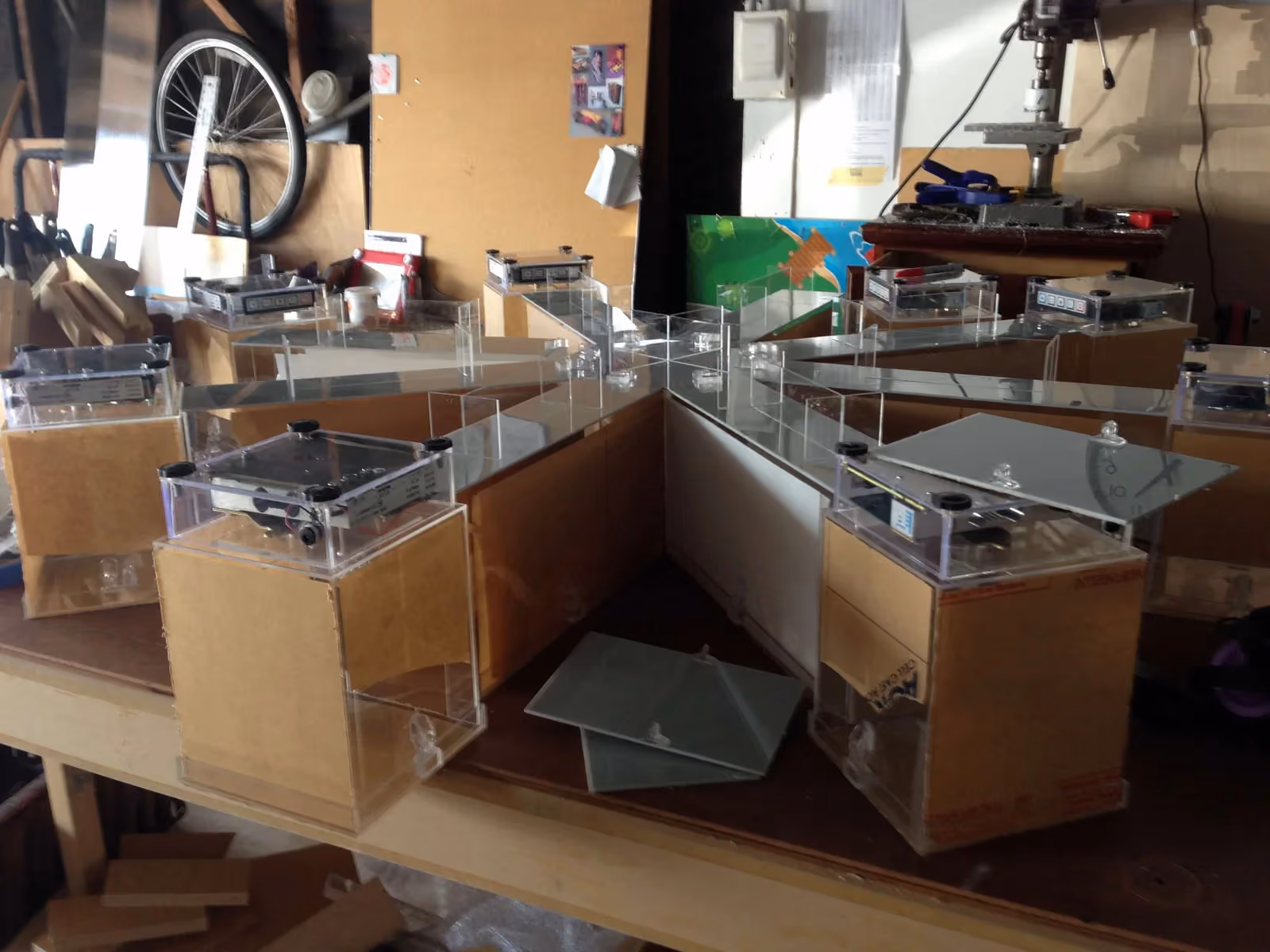 A clear acrylic eight-arm radial maze on a wooden workbench, each arm ending in a box topped by a clear case holding circuit boards