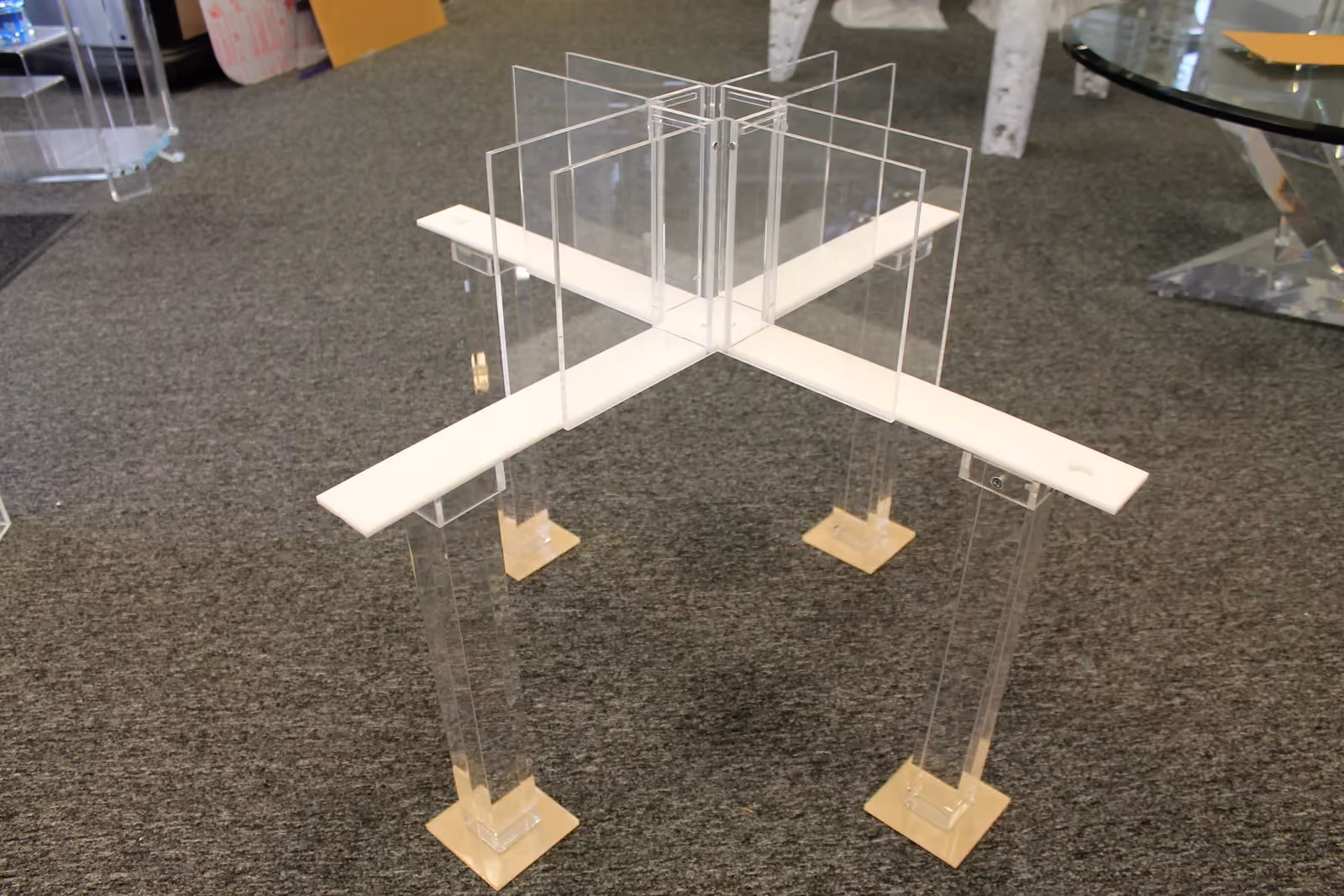A plus-shaped maze raised on four clear acrylic legs, its white arms meeting at a center enclosed by tall clear panels