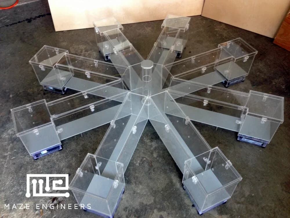 A clear acrylic eight-arm radial maze with a goal box at the end of each arm, on a concrete workshop floor