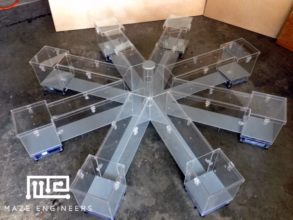 A clear acrylic eight-arm radial maze with a goal box at the end of each arm, on a concrete workshop floor