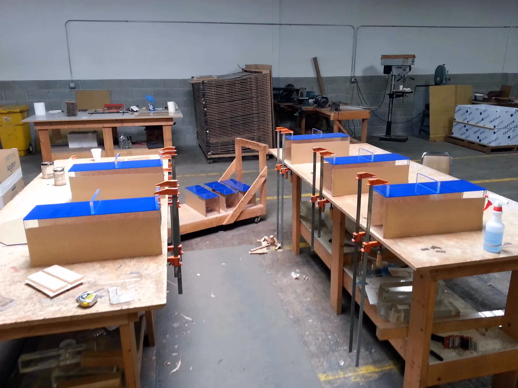 Workbenches holding maze parts with blue acrylic tops, glued and held in orange bar clamps