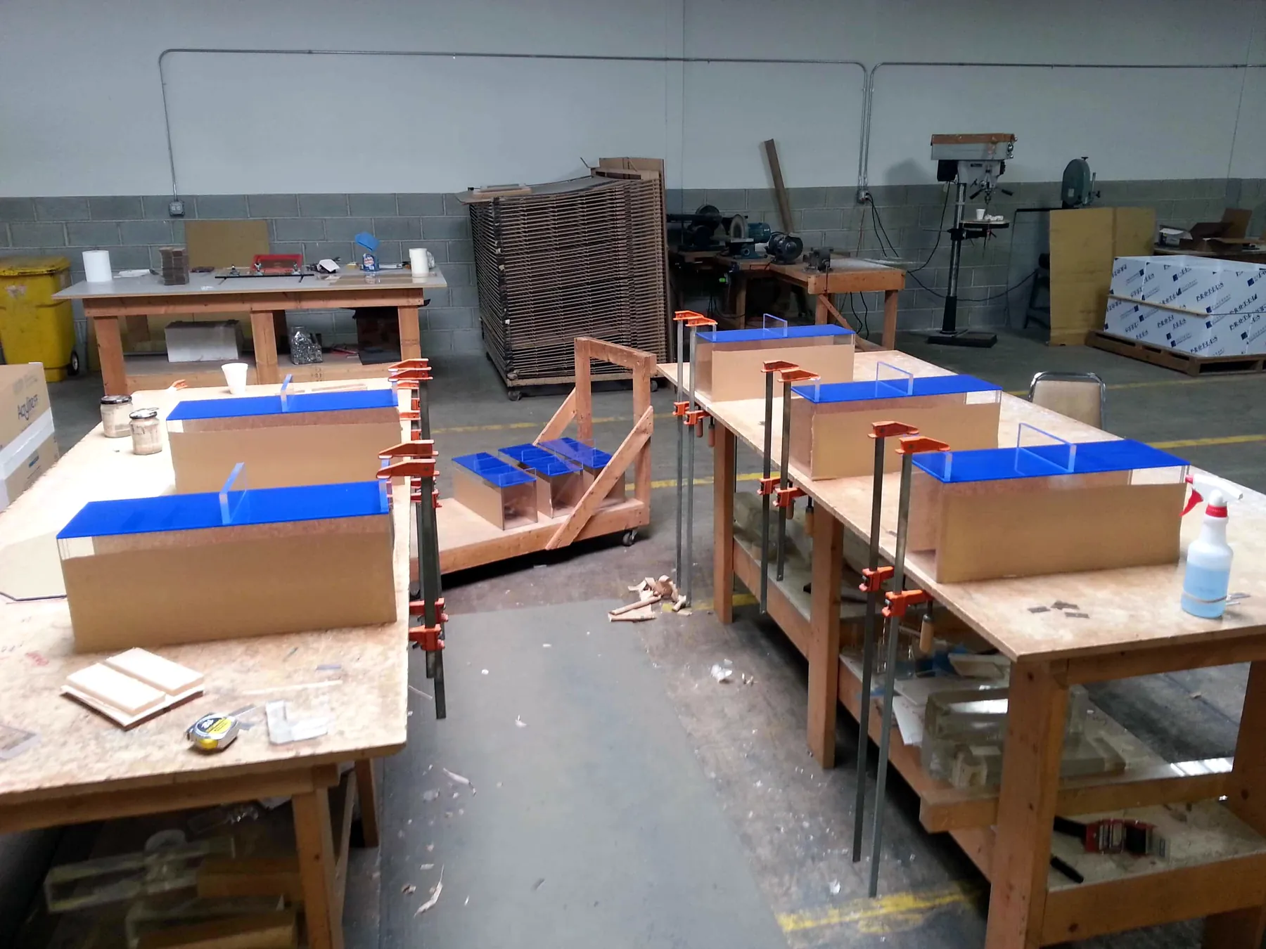 Workbenches holding maze parts with blue acrylic tops, glued and held in orange bar clamps