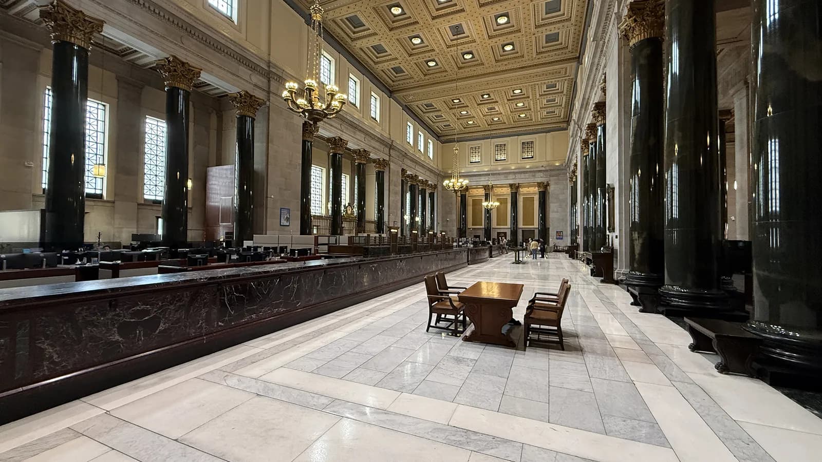 Marble columns and a coffered ceiling line the long banking hall of the Bank of Montreal head office; boxes mark 3 people near the far counters.