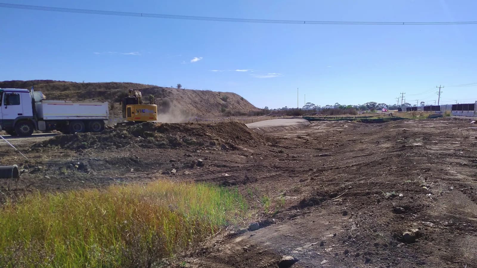 A dusty earthworks site where an excavator works next to a tipper truck; boxes mark the truck and the excavator.