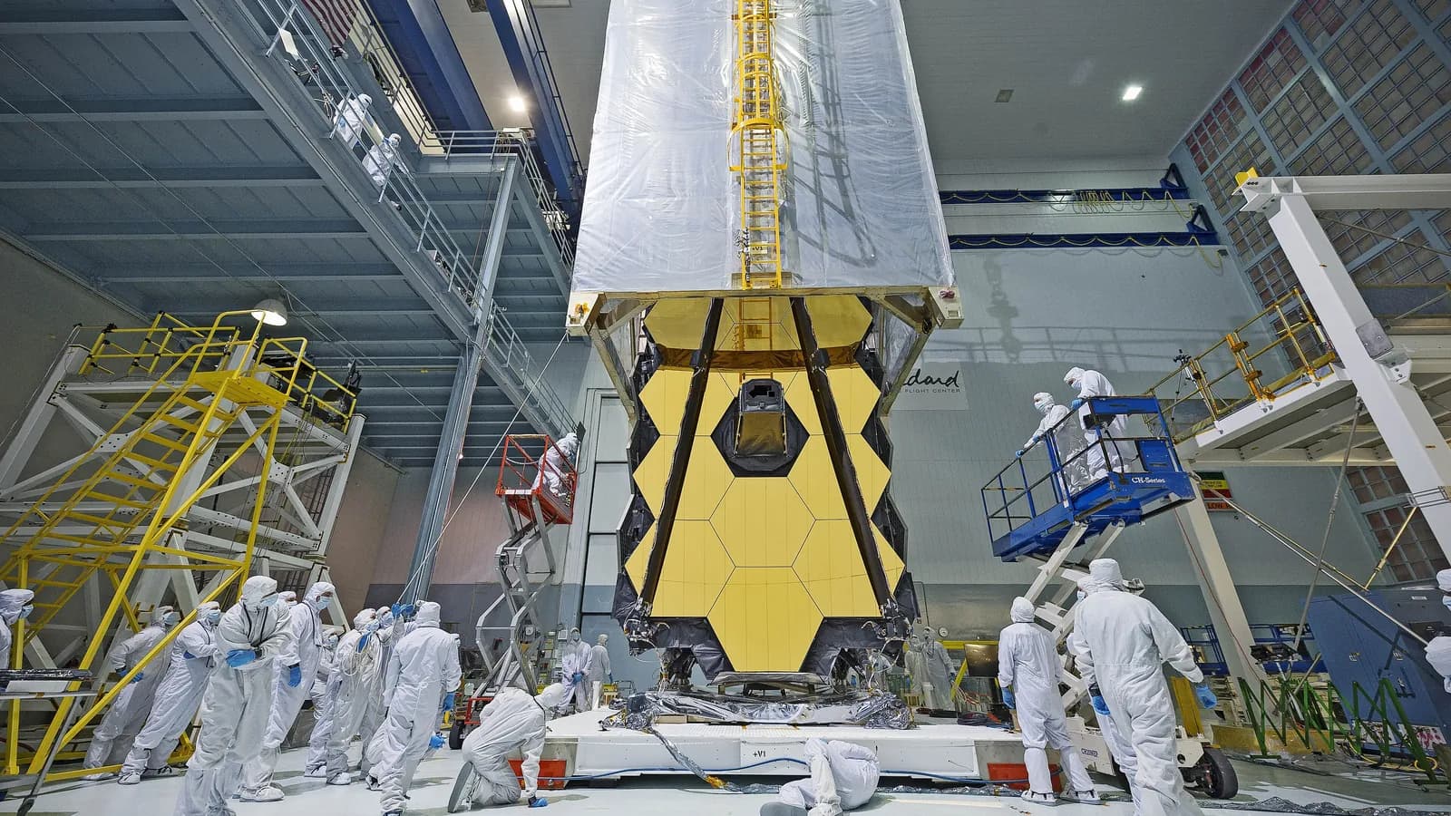 Technicians in clean room suits work around the James Webb Space Telescope in a clean room at NASA's Goddard Space Flight Center; boxes mark 19 people.