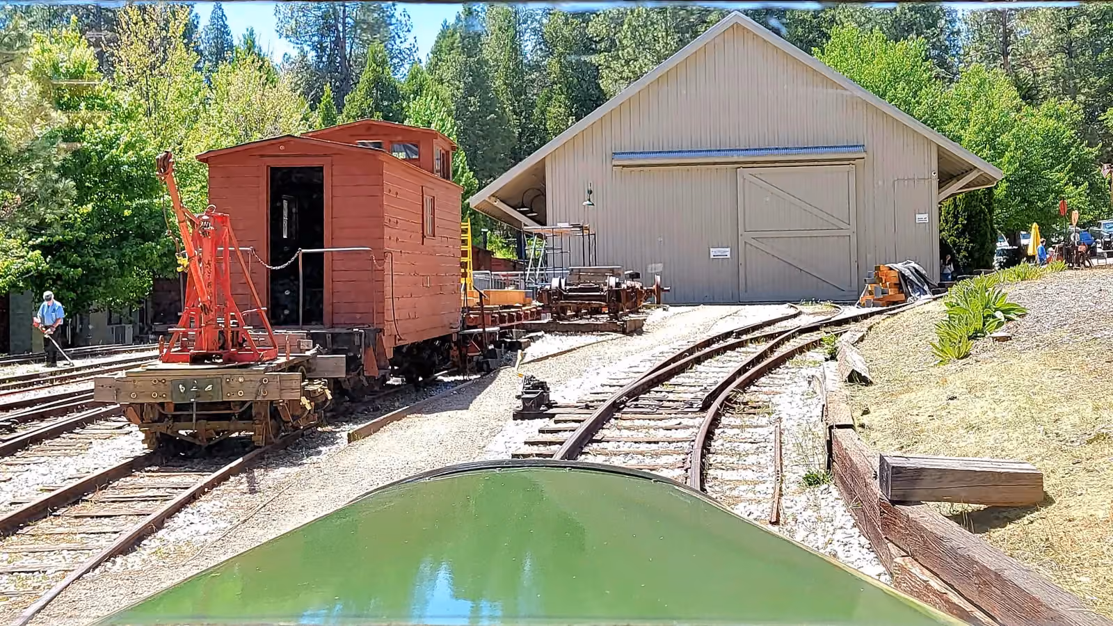 A narrow gauge railroad museum yard seen from the cab of a rail bus, with a restricted zone drawn over the yard tracks; boxes mark three people, and the man standing on the tracks inside the zone is flagged.