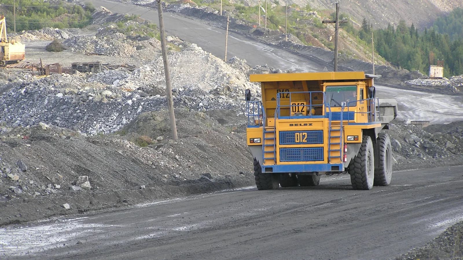 A yellow haul truck drives along a mine road near Vershina Tei in southern Siberia; boxes mark the truck, its driver and an excavator in the background.