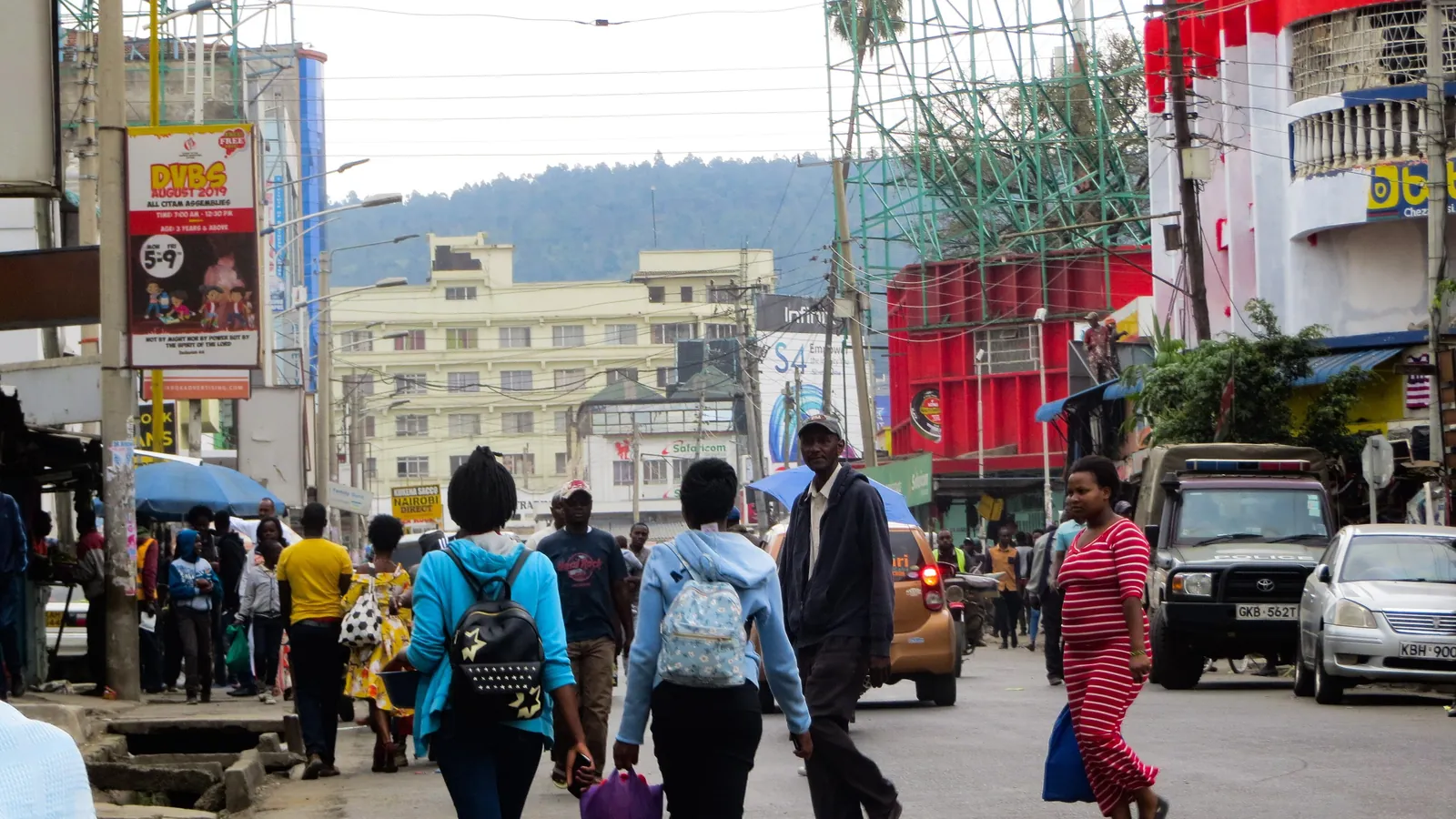 A busy shopping street in Nakuru, Kenya, with people walking between shops and parked cars; boxes mark 20 pedestrians.