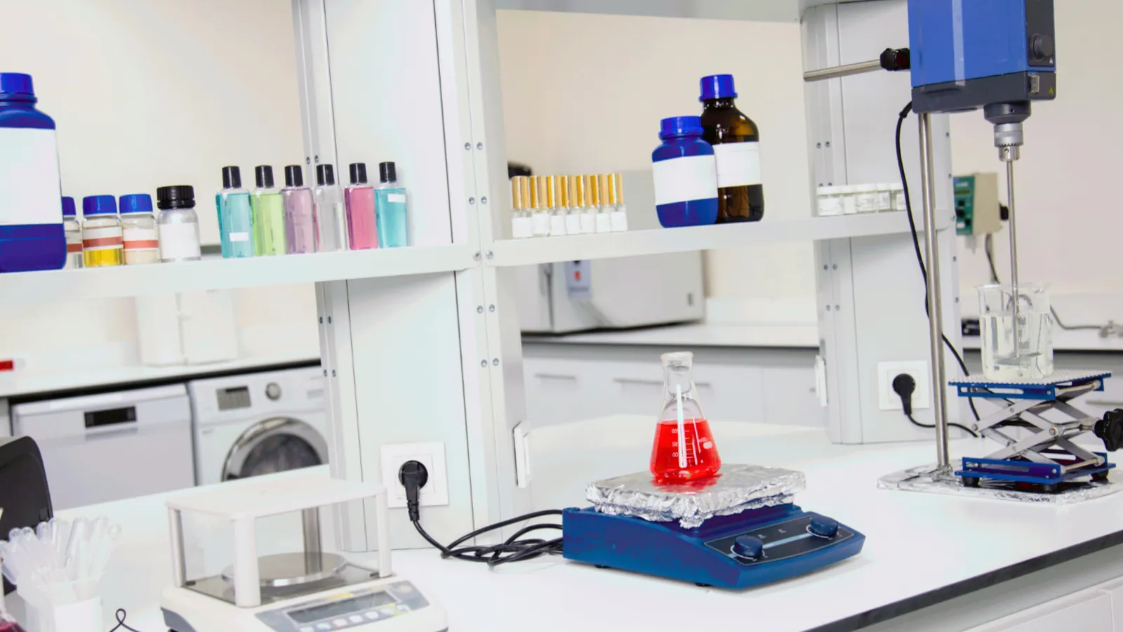 Reagent bottles line the shelves of a biotech lab above a stirrer and a flask of red liquid; boxes mark thirteen bottles.