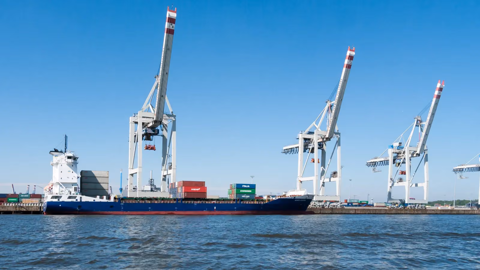 Quay cranes stand over a container terminal in Hamburg with a small container ship in the foreground; boxes mark 3 gantry cranes.