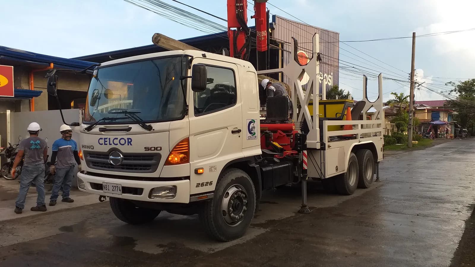 A line crew's boom truck parked under overhead cables in Cabanatuan, Philippines; boxes mark the truck, three crew members, a person down the street and one hard hat.