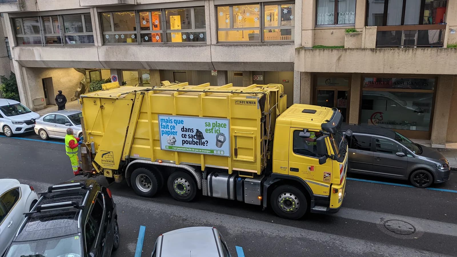 Seen from above, a yellow garbage truck stops on a street while a worker in high visibility clothing loads it from behind; boxes mark the truck, the worker and a passerby.