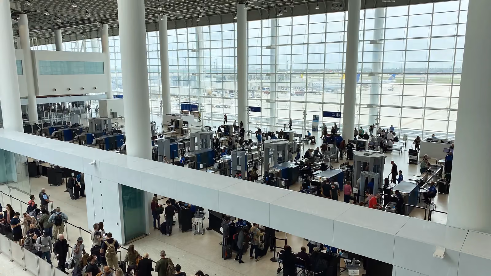 Travelers wait in line and pass through the scanners at an airport security checkpoint in New Orleans, seen from an upper floor; boxes mark 19 people, 4 backpacks, a bag and a suitcase.
