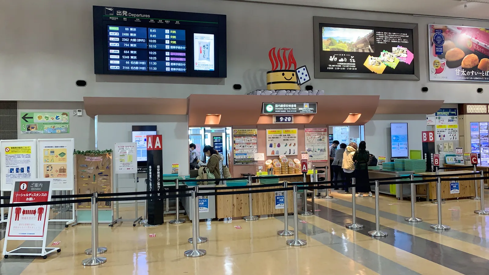 Travelers place their belongings in trays at the domestic security checkpoint of Oita Airport in Japan; boxes mark 6 people and a bag.