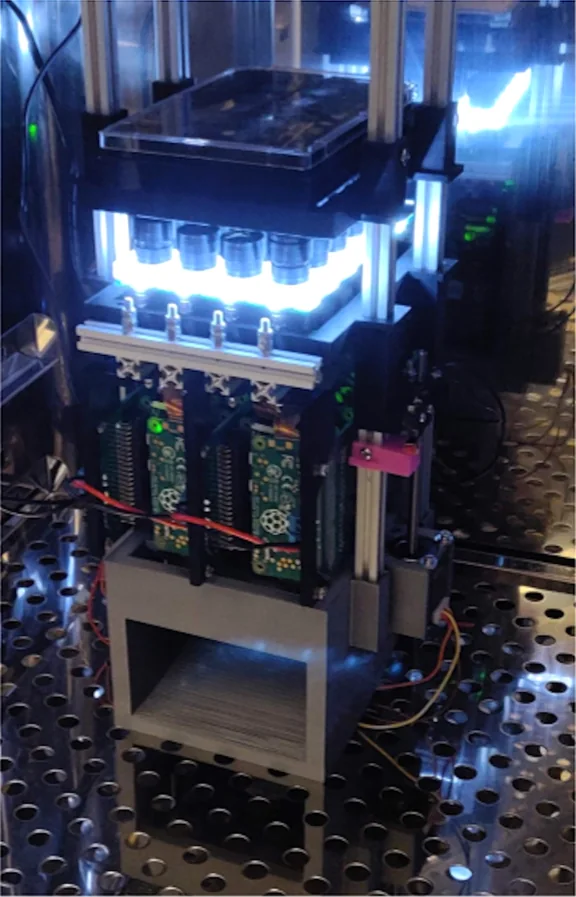 Photo of the Picroscope inside a cell culture incubator, a tower of cameras and circuit boards under a lit plate holder.