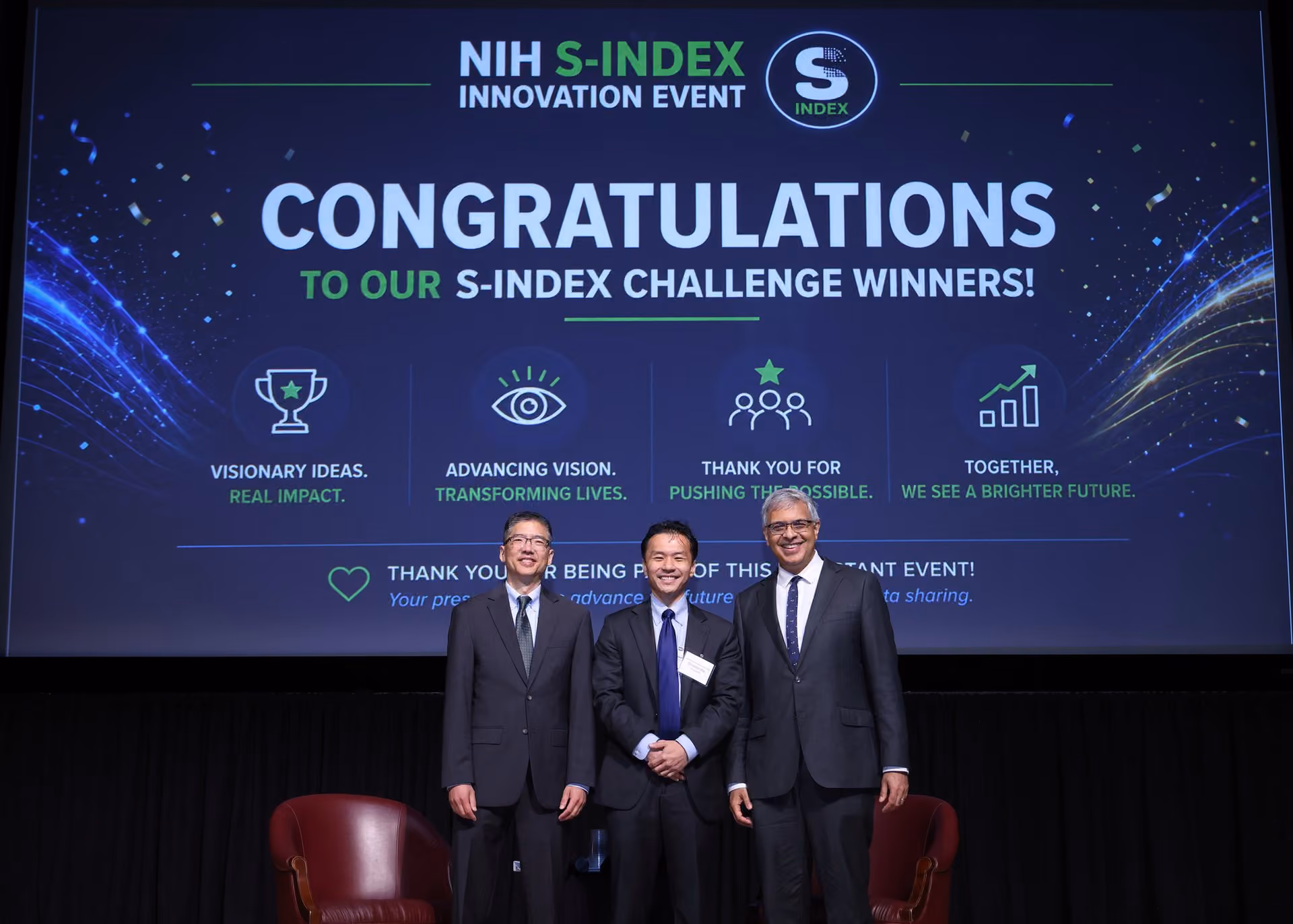 Shuhan He standing with NIH leaders on stage beneath a screen congratulating the S-Index Challenge winners