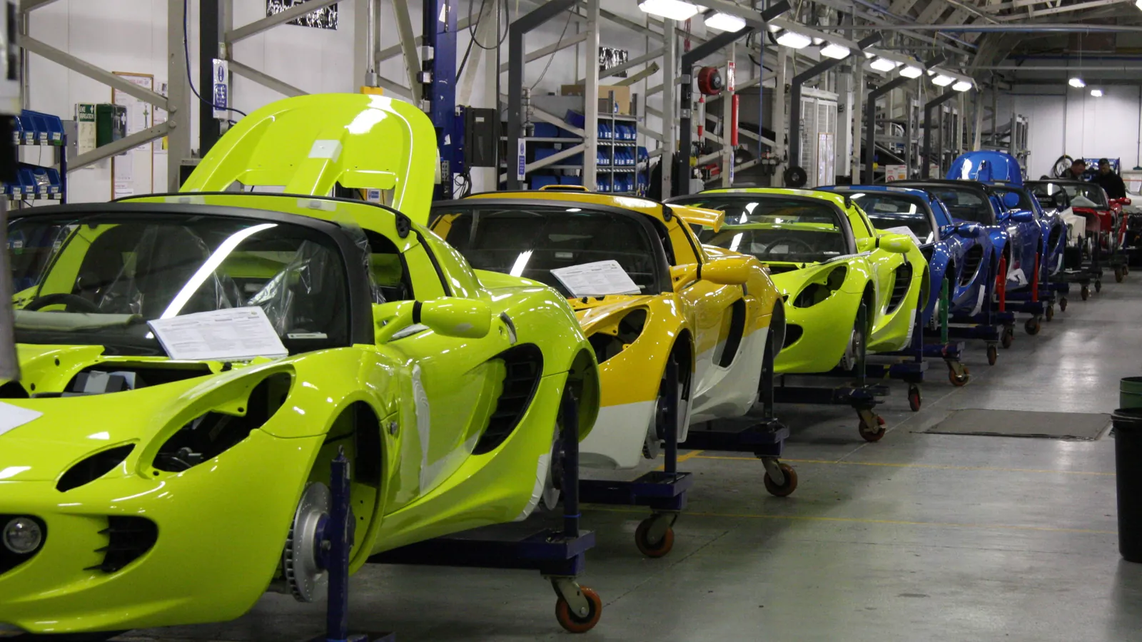 Partly built sports cars stand in a row on a final assembly line; boxes mark 4 cars and 2 people.