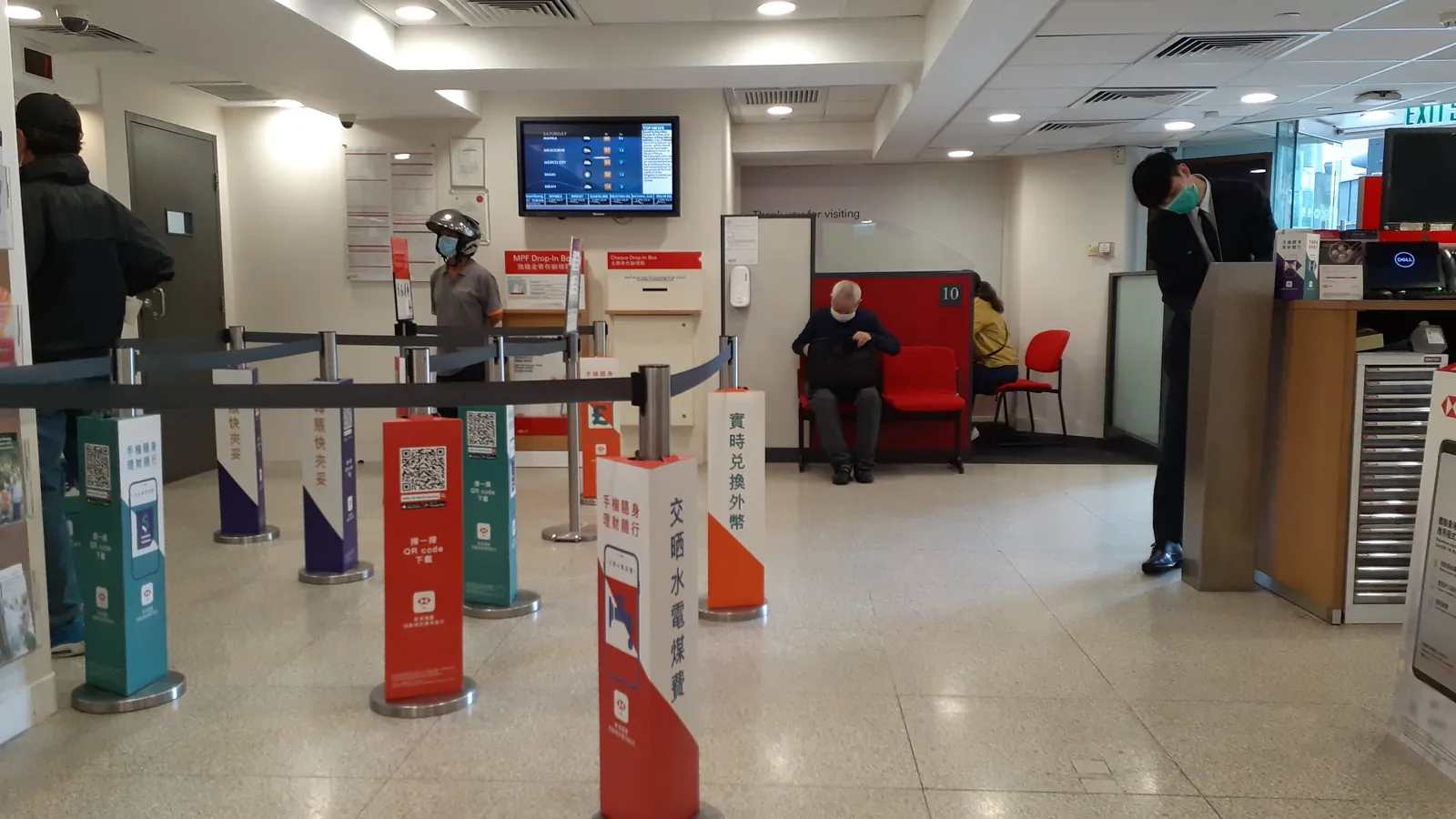 Customers wait by queue stands and service kiosks in a bank branch lobby in Sai Ying Pun, Hong Kong; boxes mark 6 people and a bag.