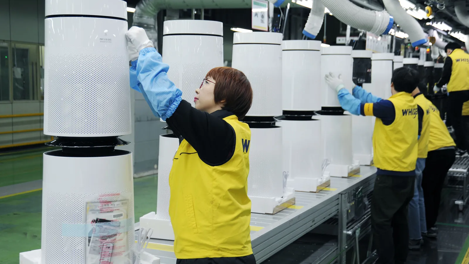 A worker in blue sleeve covers fits the top of an air purifier as others work down the line; boxes mark four workers.