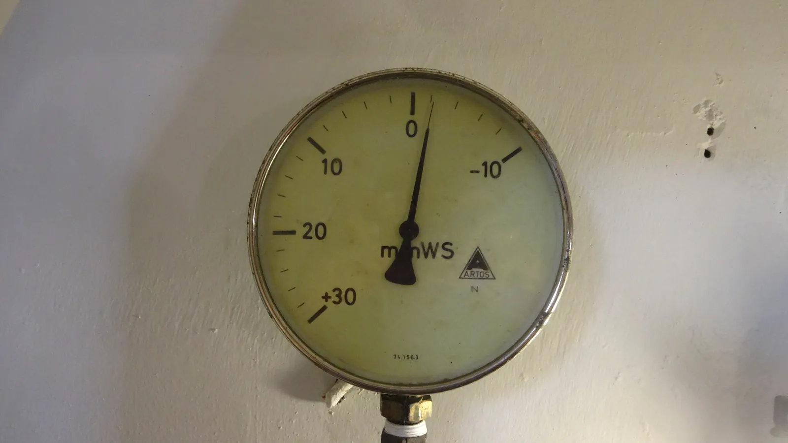 A ventilation pressure gauge on a shelter wall, its needle resting near zero; one box marks the gauge.