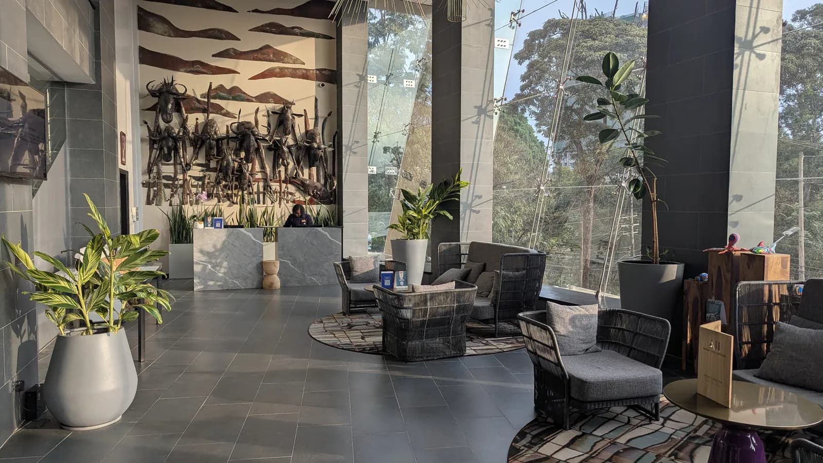 Woven armchairs face the reception desk in a bright hotel lobby; boxes mark 3 chairs and 1 person at the desk.