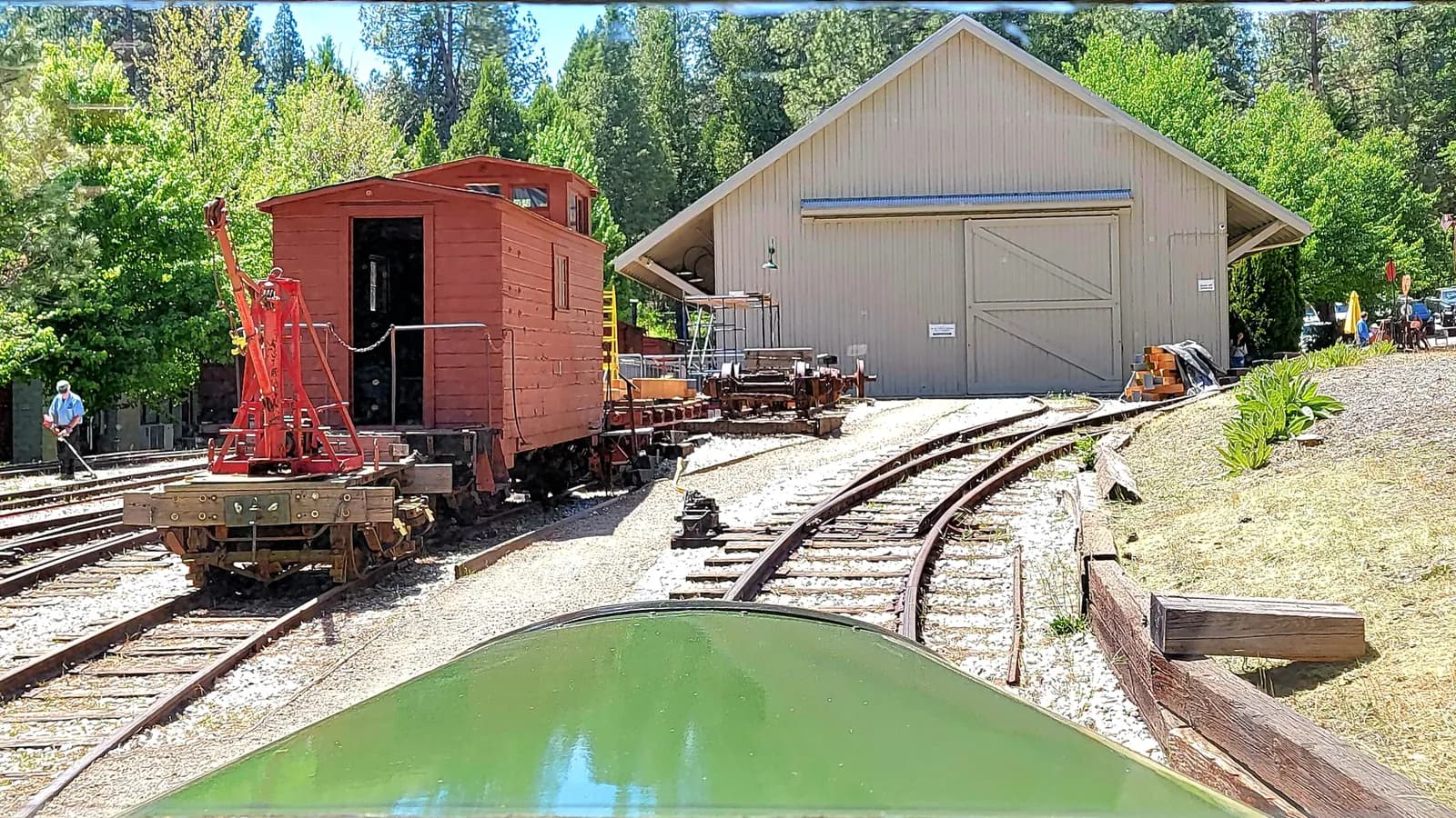 A narrow gauge railroad museum yard seen from the cab of a rail bus, with a restricted zone drawn over the yard tracks; boxes mark three people, and the man standing on the tracks inside the zone is flagged.