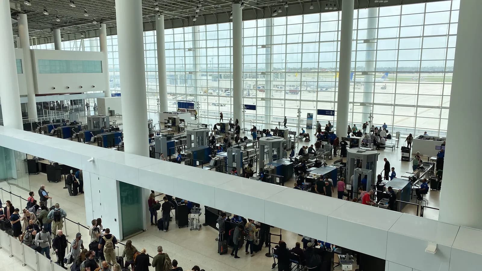 Travelers wait in line and pass through the scanners at an airport security checkpoint in New Orleans, seen from an upper floor; boxes mark 19 people, 4 backpacks, a bag and a suitcase.
