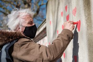 Elderly woman painting hearts on street wall - Featured image